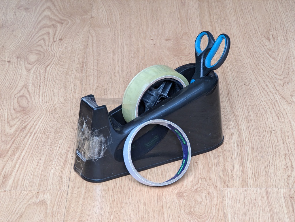 picture of a sellotape dispenser with a pair of scissors and a roll of tape leaning against it